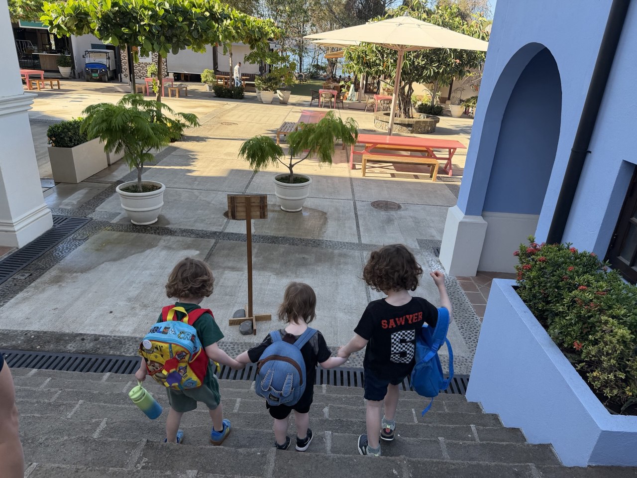 Three boys holding hands walking down stone steps with backpacks