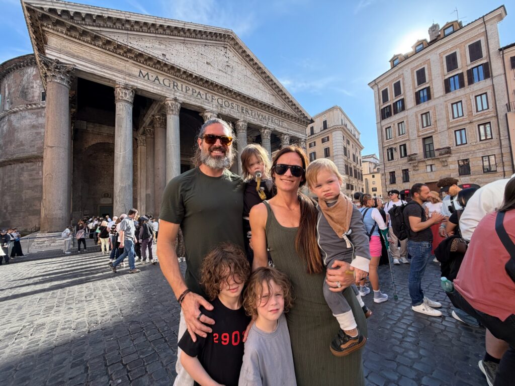 Family portrait of parents and four young boys posing in front of the Pantheon in Rome under a bright blue sky