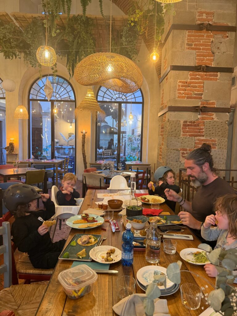 Family of six having dinner at a rustic Italian restaurant with exposed brick walls and hanging pendant lights, boys still in scooter helmets
